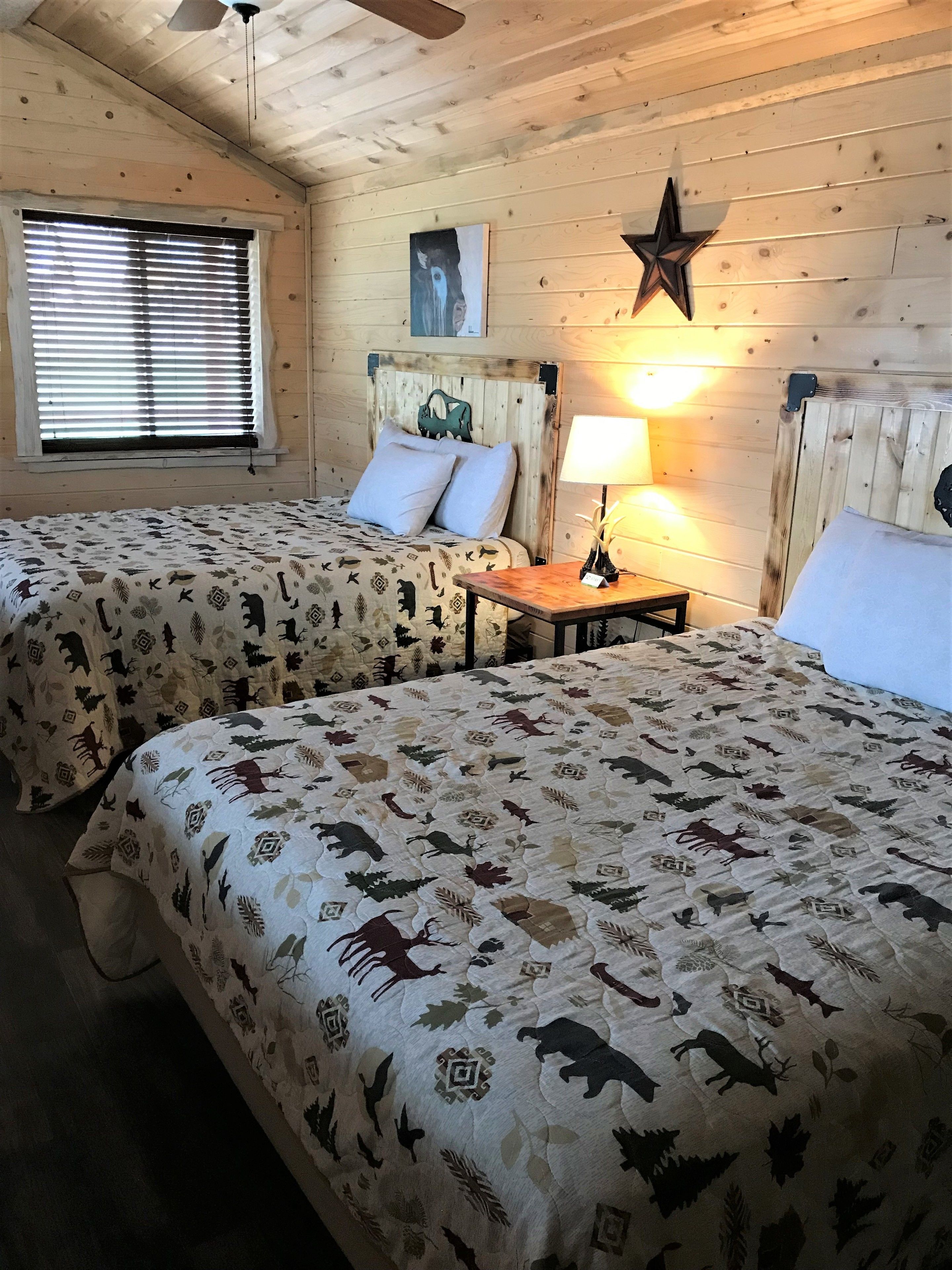 Une chambre de style cabane avec deux lits, une décoration en forme d’étoile sur le mur et une fenêtre avec des stores.