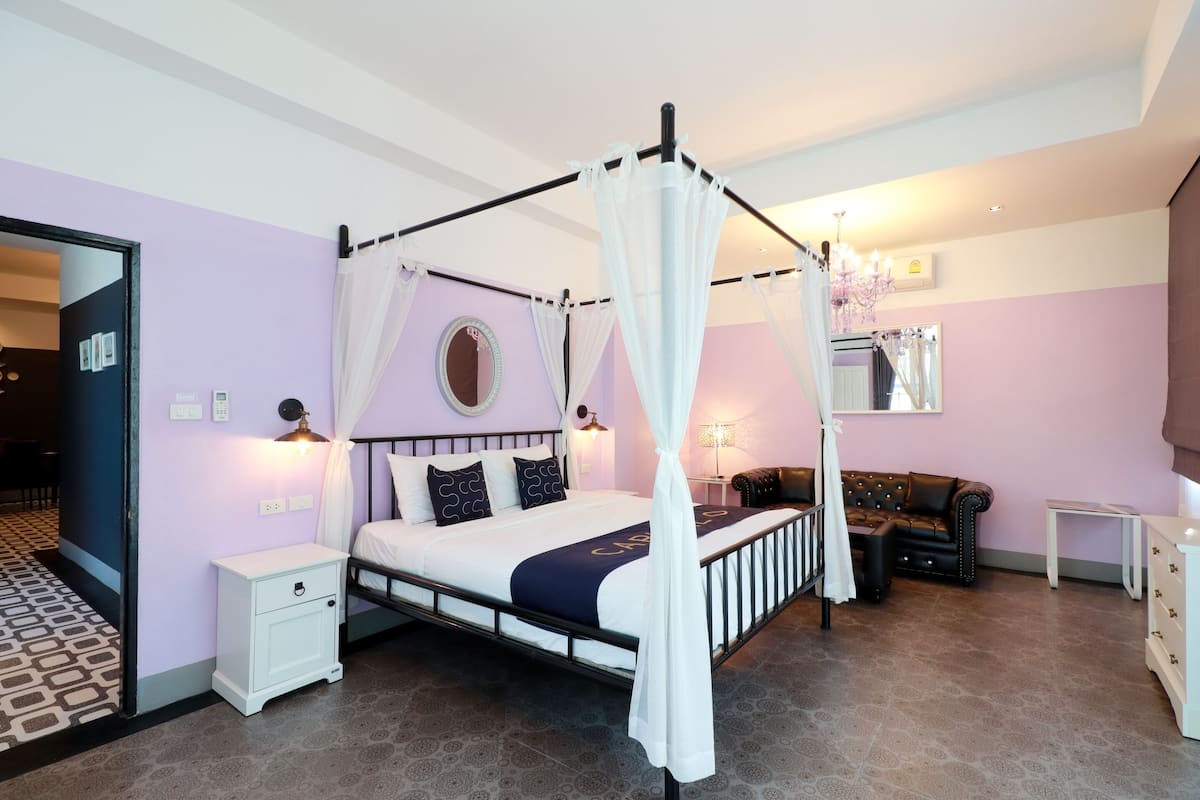 A bedroom with a four-poster bed, a nightstand, a dresser, a mirror, and a chandelier.