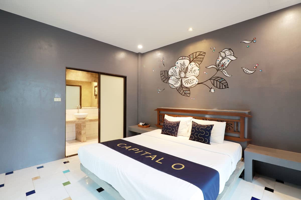 A modern hotel room with a large bed, a nightstand, a wooden headboard, and a wall mural.