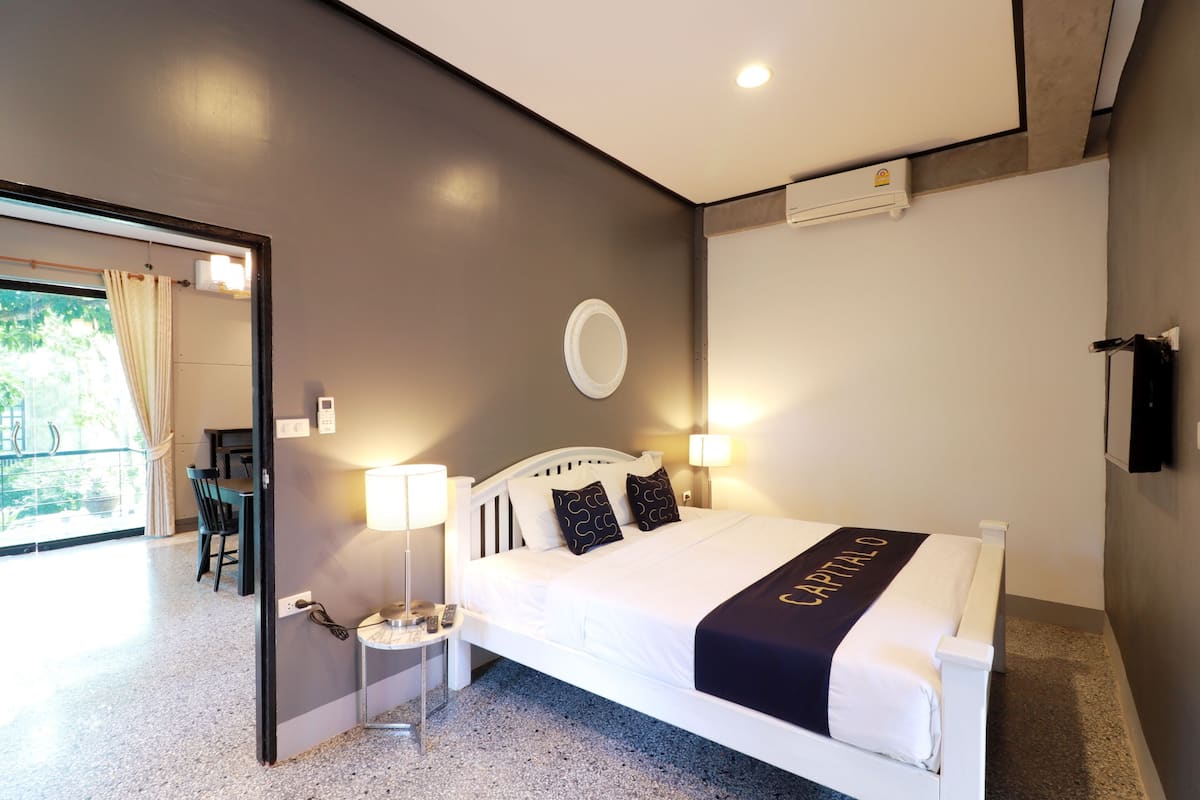 A modern hotel room with a bed, bedside lamps, a round mirror, and a view of the outside.