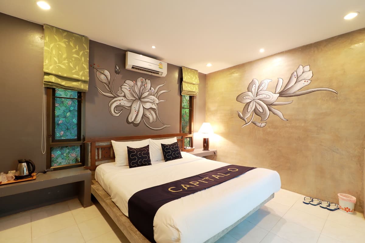 A hotel room with a bed, a nightstand, a lamp, a window with a floral pattern, and a wall with a floral mural.