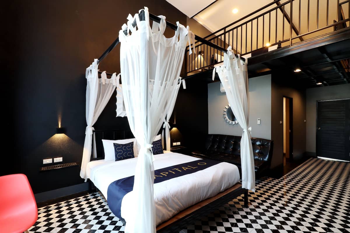 A four-poster canopy bed with a black and white checkered floor, a red chair, and a black leather sofa.