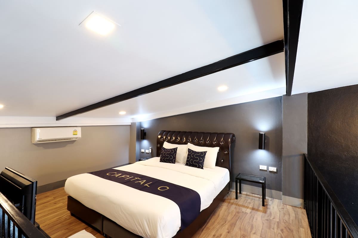 A modern hotel room with a large bed, a small bedside table, and an air conditioning unit on the wall.