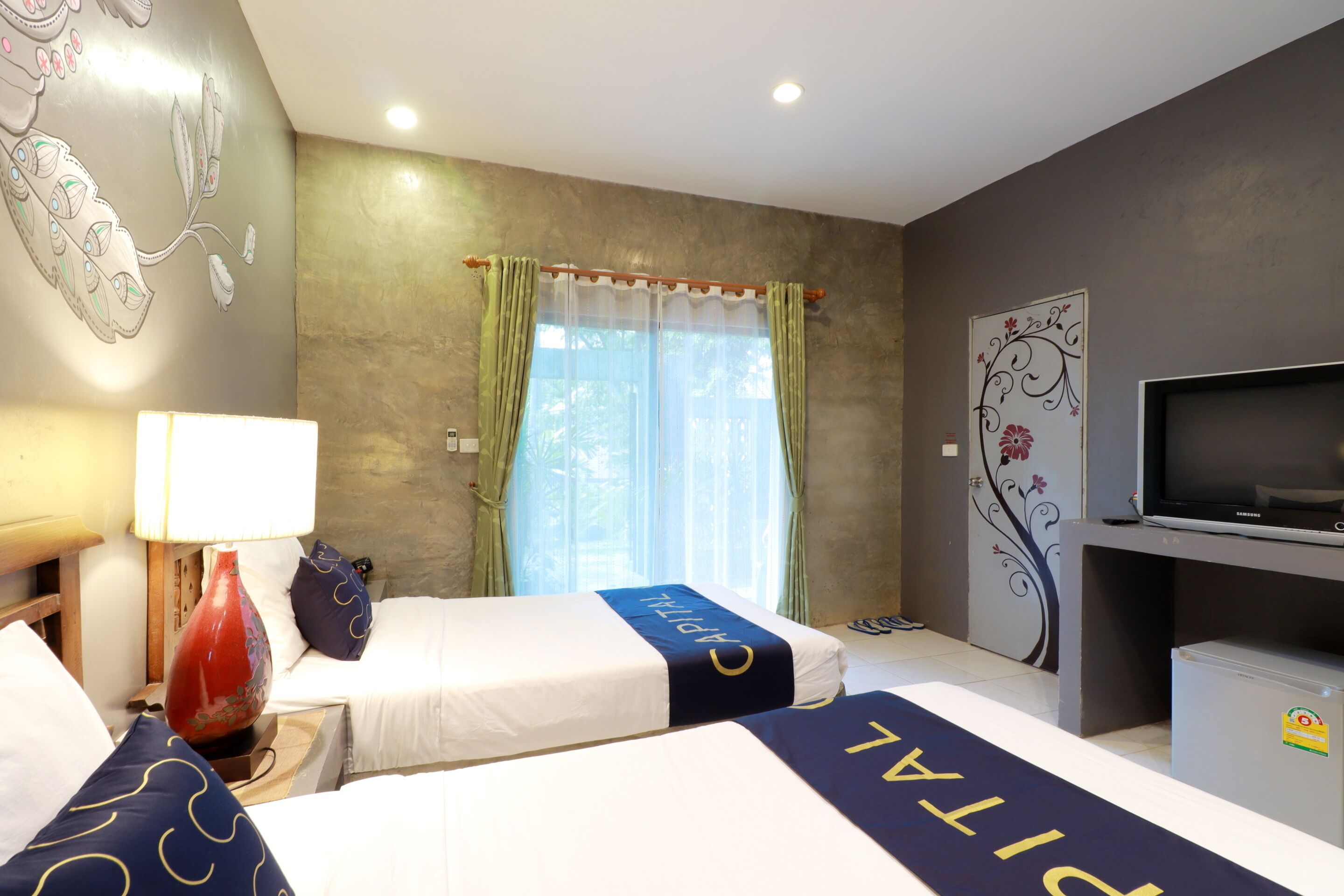 A hotel room with two beds, a TV, a small refrigerator, and a window with curtains.