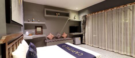 A hotel room with a bed, a television, a small desk, and a window with curtains.