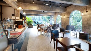 A cafe with a barista station, seating area, and large windows with a view of greenery. - Capital O 464 At Nata Chiangmai Chic Jungle (Mae Rim)