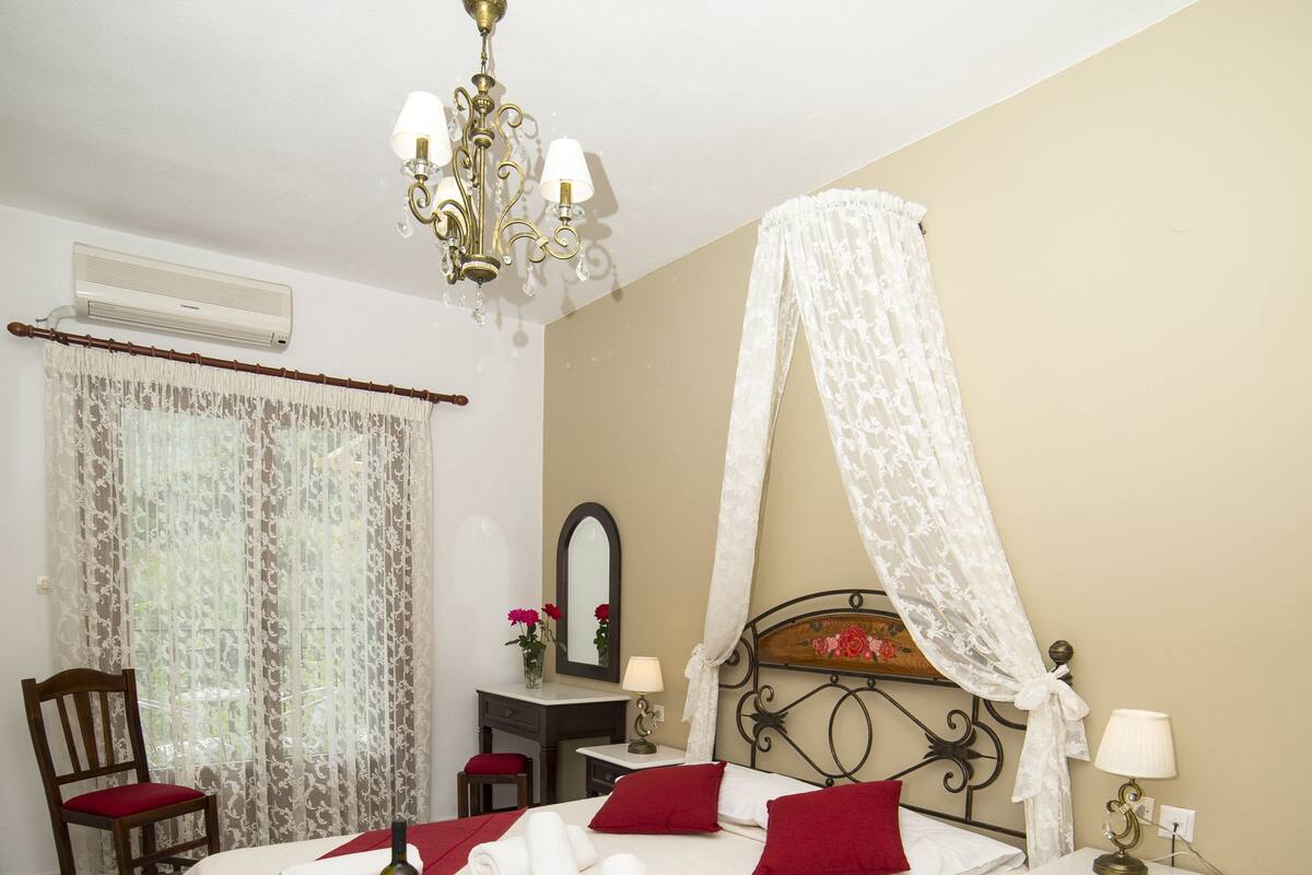 A neatly arranged bedroom with a bed, bedside tables, a chair, a mirror, and a chandelier.