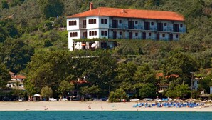 Un immeuble à plusieurs étages, doté d’un toit rouge, situé sur une colline surplombant une plage aux eaux bleues.