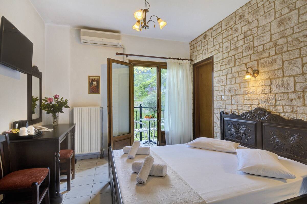 A hotel room with a bed, a desk, a chair, a mirror, and a view of the outdoors.
