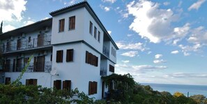 Edifici blanc de dos pisos amb balcons, una antena parabòlica i vista al mar.