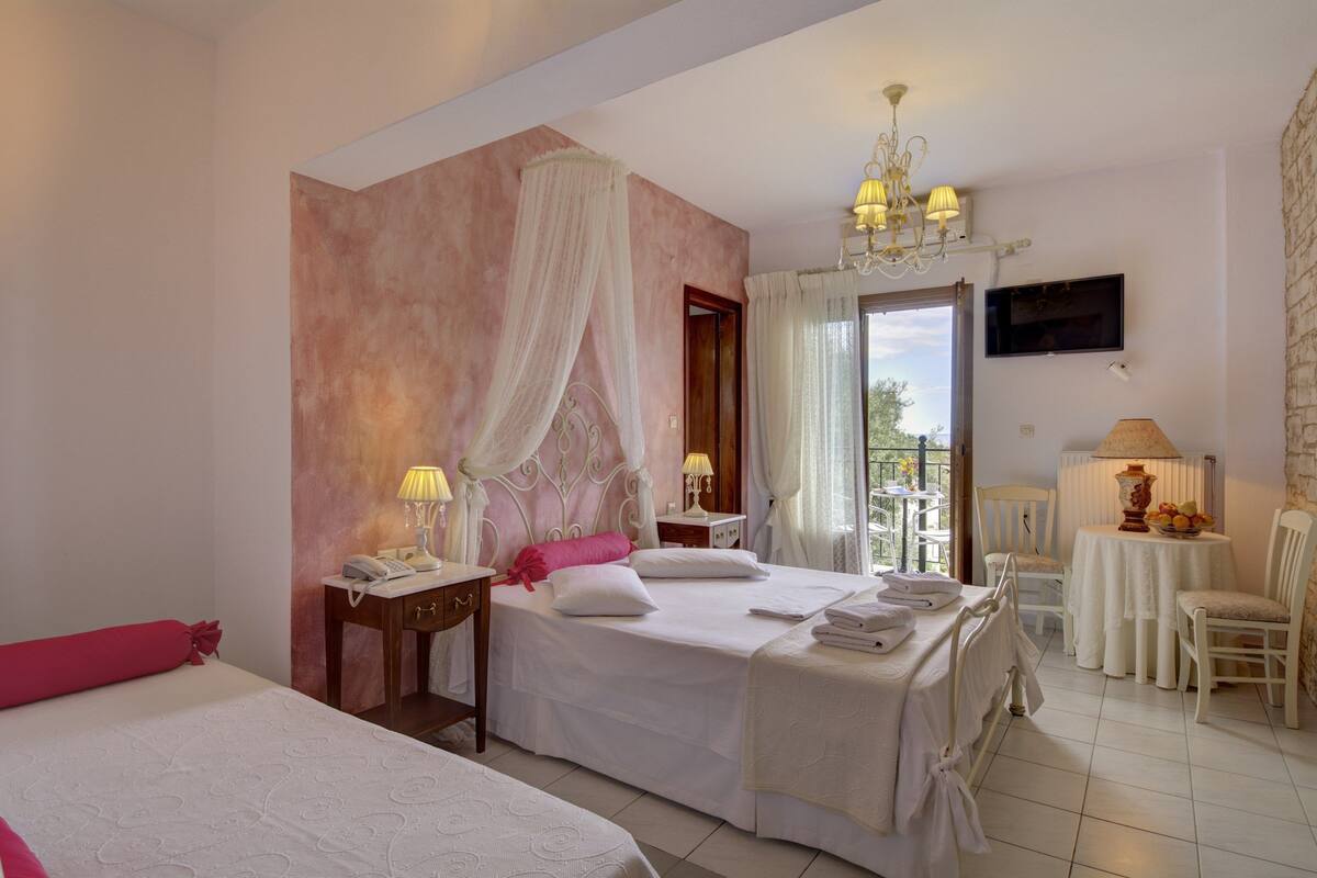 A hotel room with a bed, bedside tables, a chair, a small table with a lamp, and a TV on the wall.