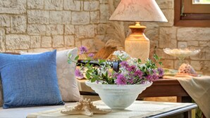 Une pièce avec un mur en pierre, une lampe, un vase de fleurs, un coussin et un objet décoratif posé sur une table.