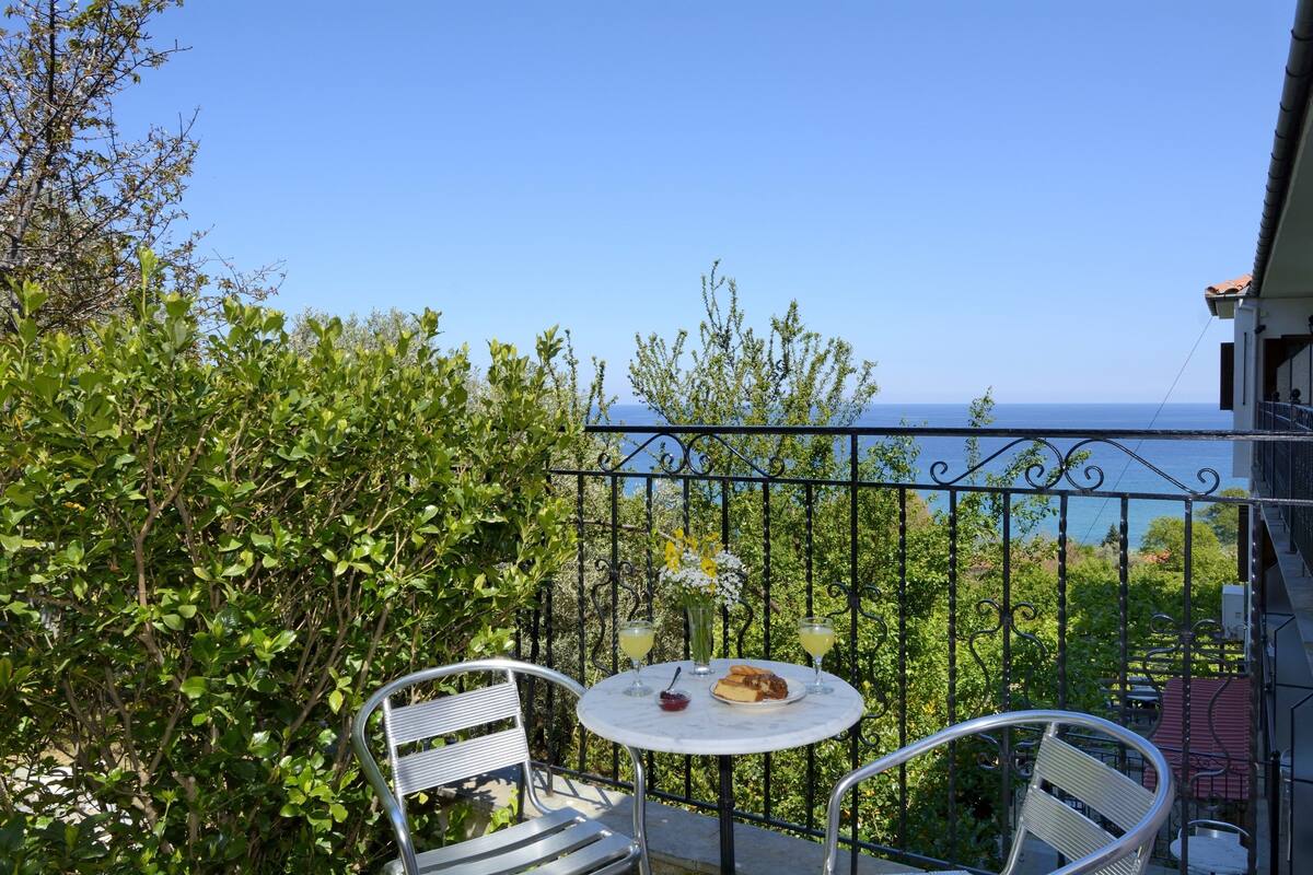 A balcony with a table and chairs, overlooking a scenic view of the sea.