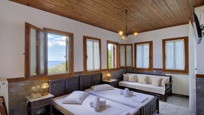Une chambre d’hôtel avec deux lits, un canapé, un mur en pierre et de grandes fenêtres avec des rideaux.