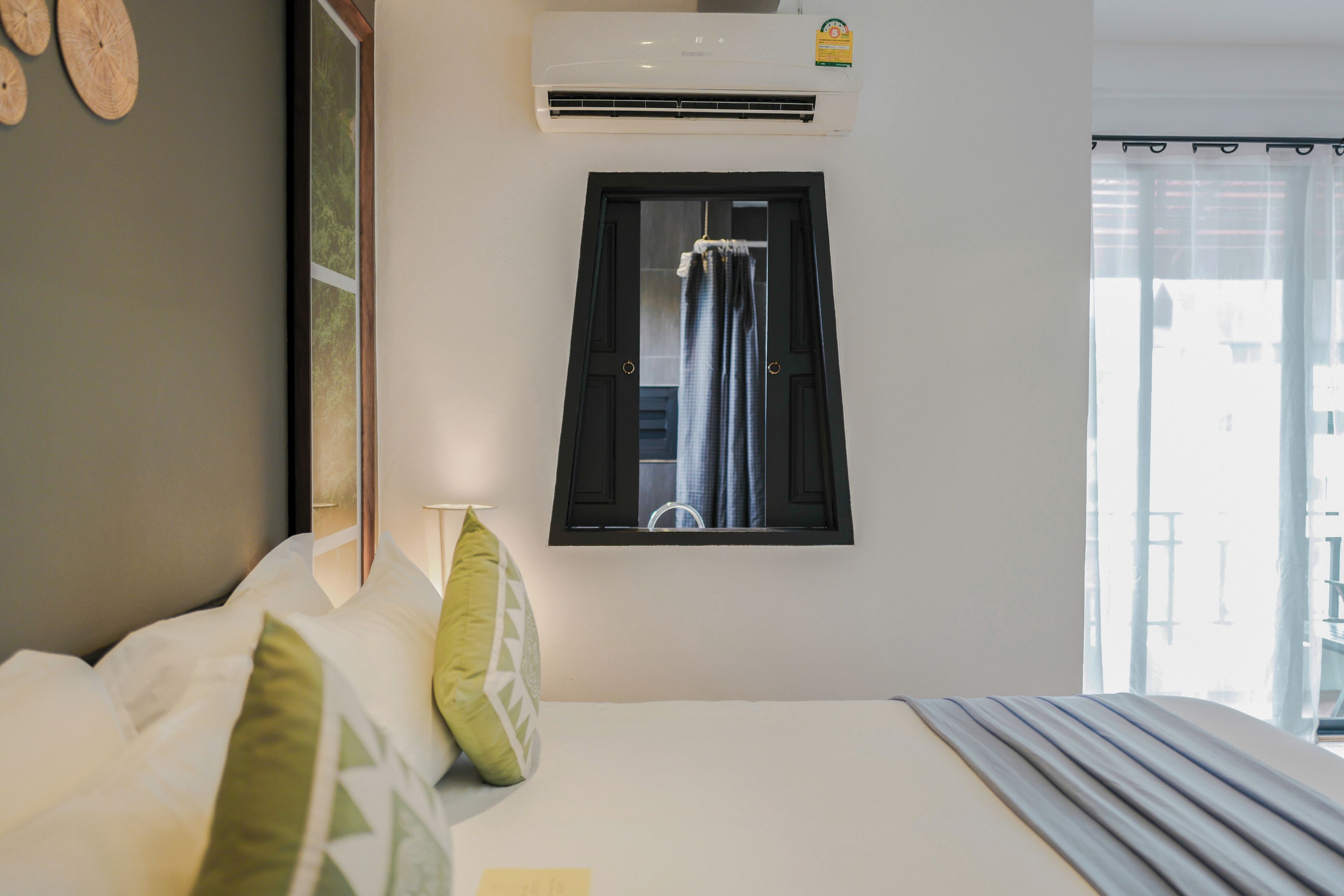 A hotel room with a bed, a window with curtains, an air conditioning unit, and a view of the outside.