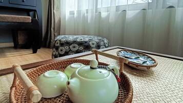 A room with a wicker tray holding teapots and a tea brush, a patterned cushion, and a small table with a tray.