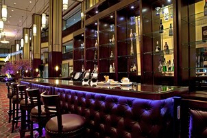 A bar area with a tufted leather bench, bar stools, and shelves displaying liquor bottles.