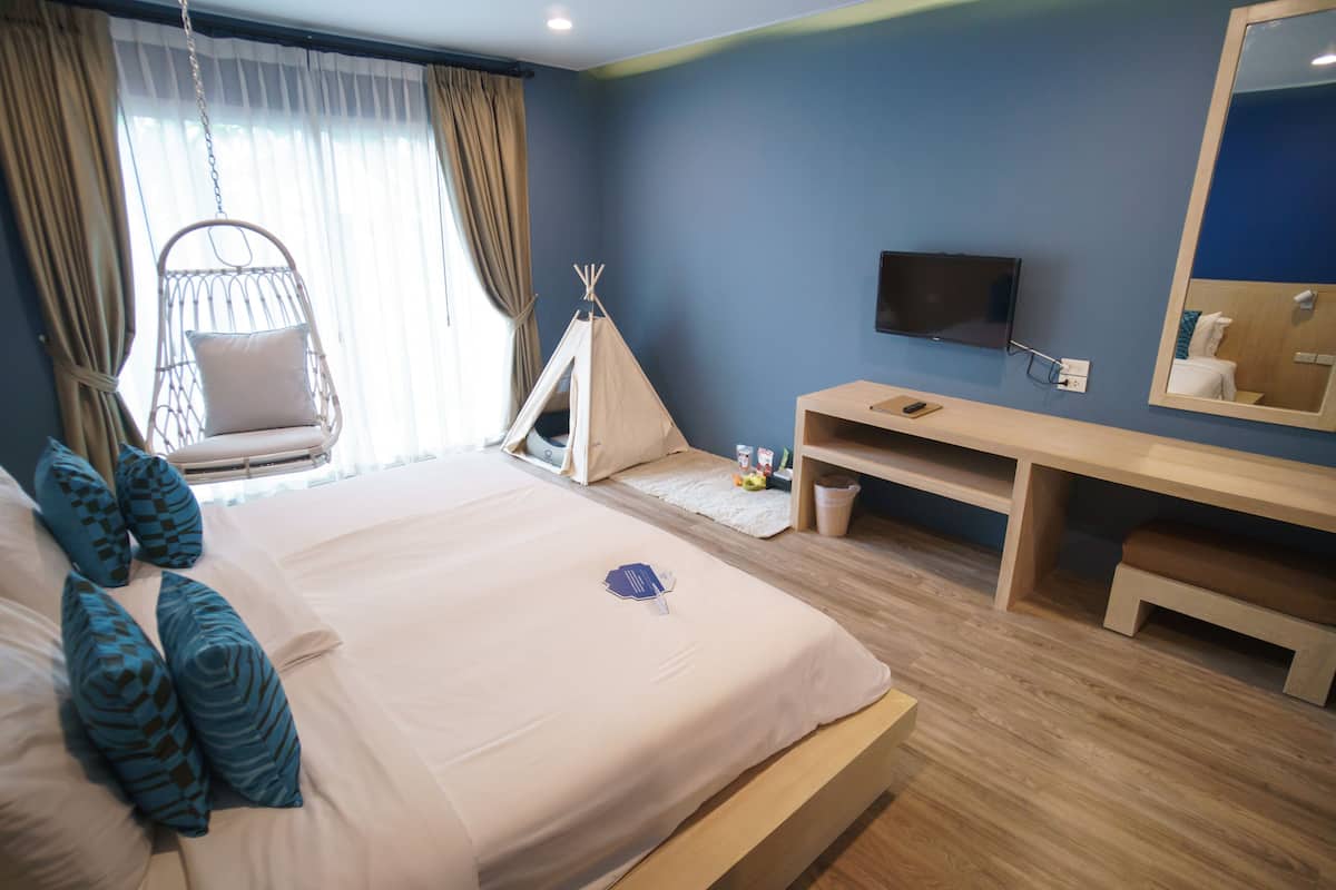 A bedroom with a bed, a hanging chair, a TV, a mirror, and a desk.