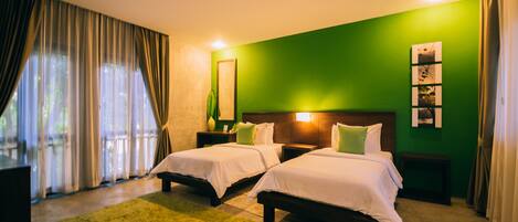 A hotel room with two beds, a green wall, a large window with curtains, and a green rug.
