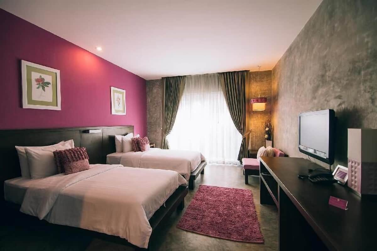 A hotel room with two beds, a desk with a computer, a TV, and a window with curtains.