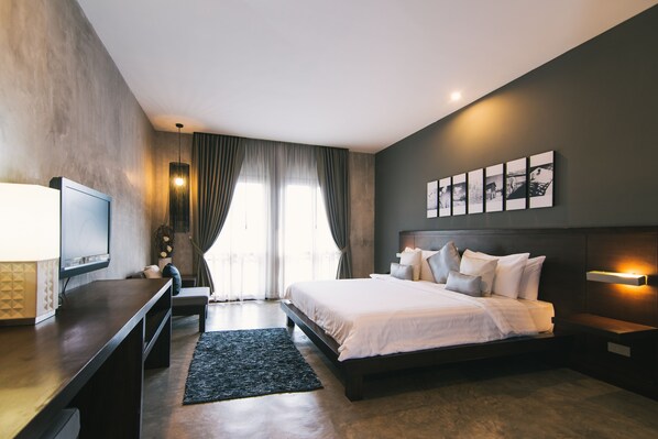 Quarto de hotel moderno com cama grande, televisão de tela plana, escrivaninha e uma ampla janela com cortinas.