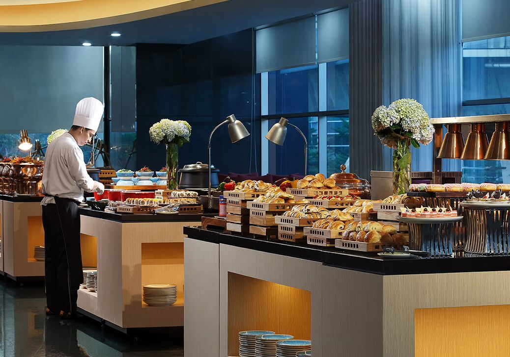 A buffet setup with various food items and a chef preparing food.