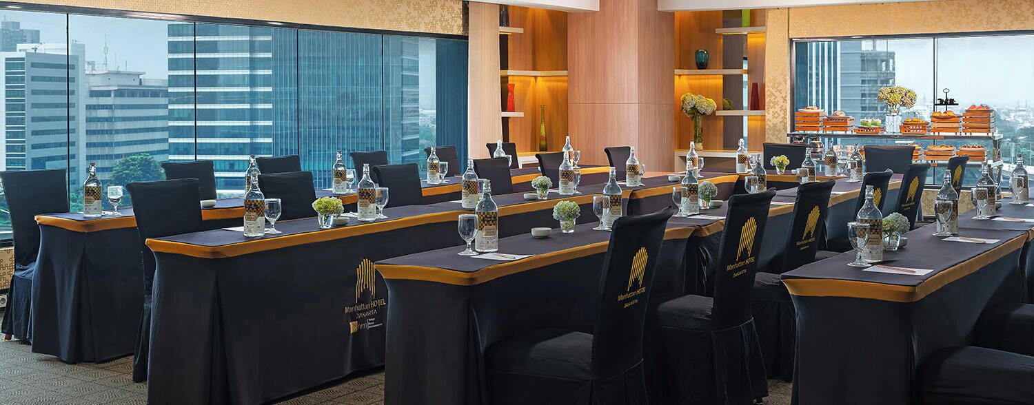 A conference room with tables set for a meeting, equipped with glassware and centerpieces.