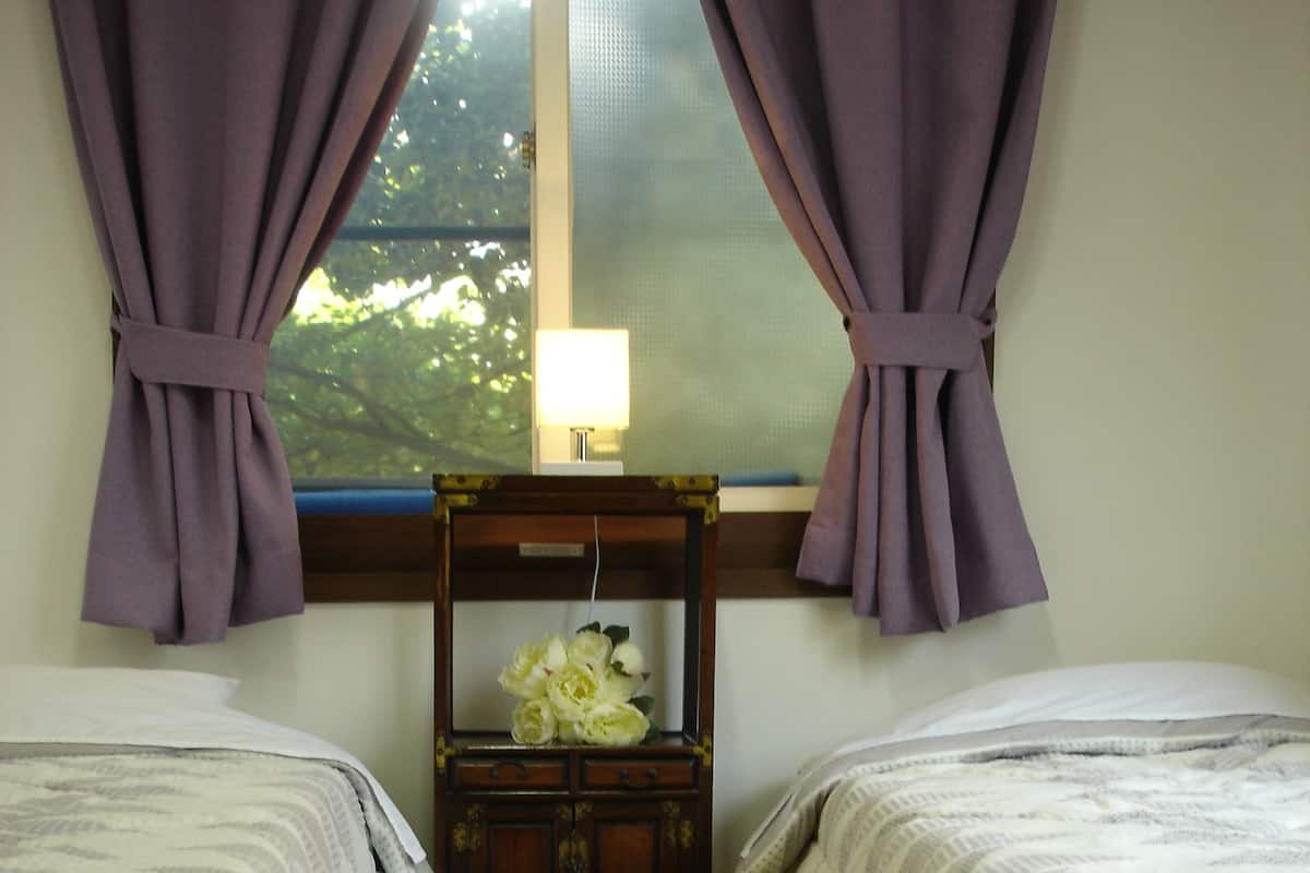 A bedroom with two beds, a small wooden cabinet with flowers, and a window with curtains.