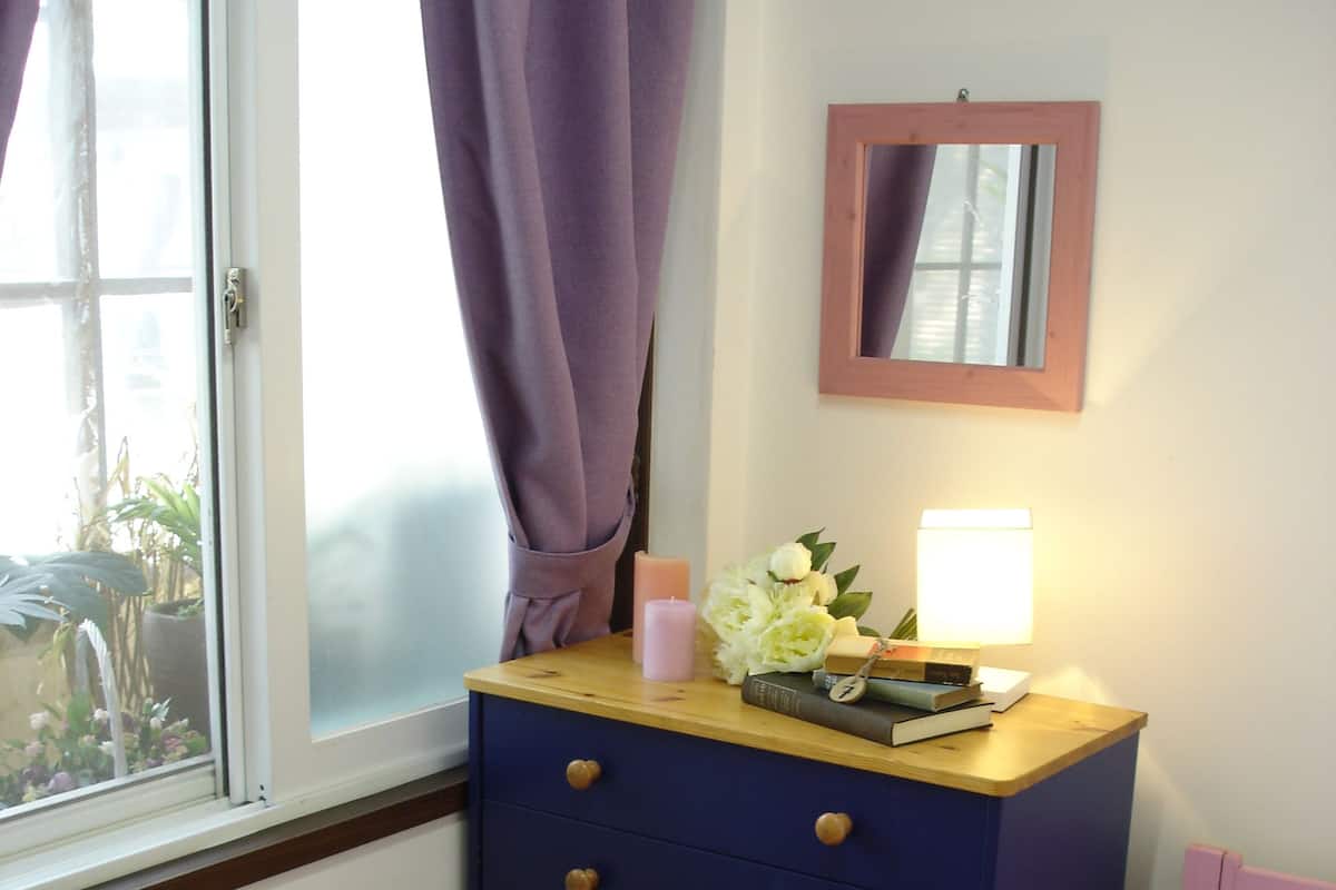 A bedroom with a wooden dresser, a bedside table with a lamp, a mirror, and a pink bedspread.