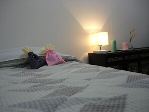 A bed with a white quilt, two small bags on it, a nightstand with a lamp, and a vase with flowers. - iCOS Guesthouse 2 for Female - Hostel (Seoul)