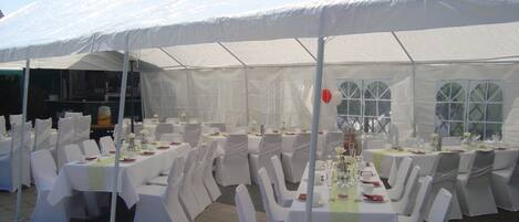 Zona de comedor al aire libre con carpas, manteles blancos y sillas, preparada para un evento formal.