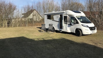 A white motorhome parked in a grassy area with a house in the background.