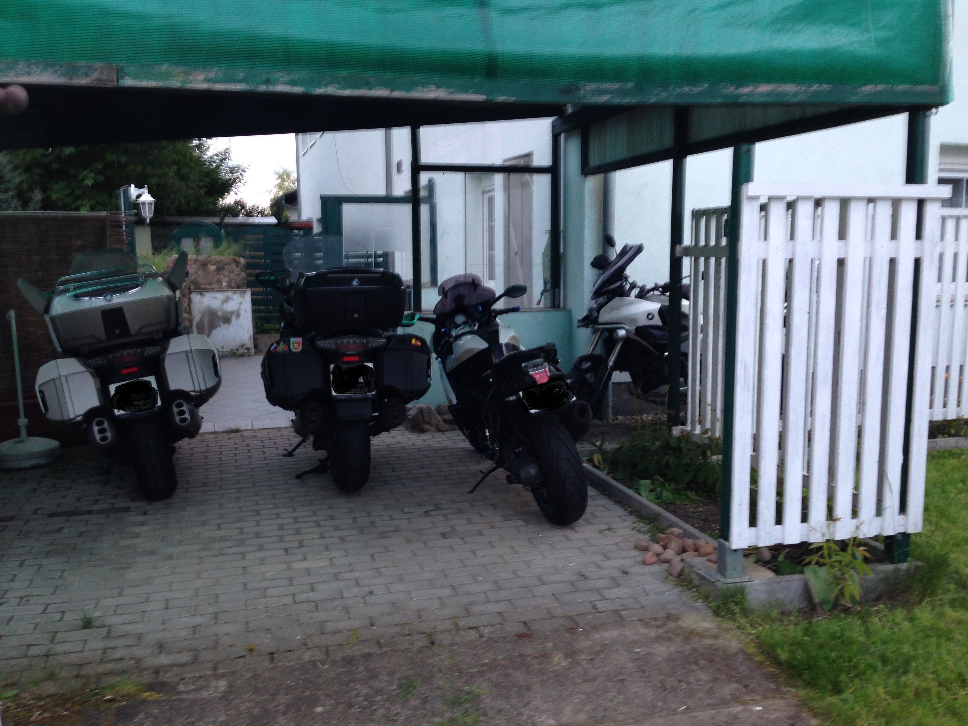 A covered parking area with three motorcycles parked under a green canopy.