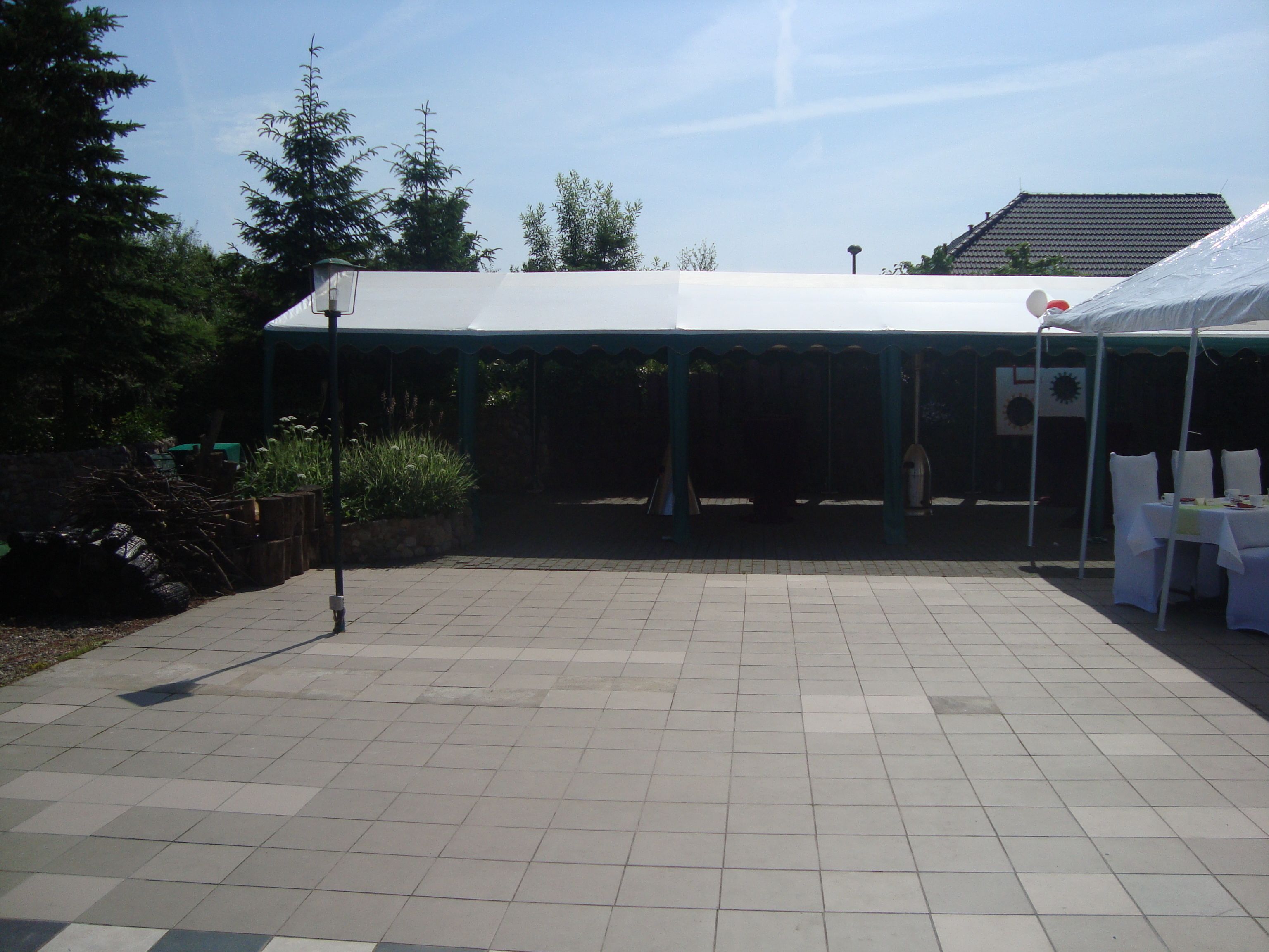 A covered outdoor area with a tiled floor, a white tent, and a building in the background.