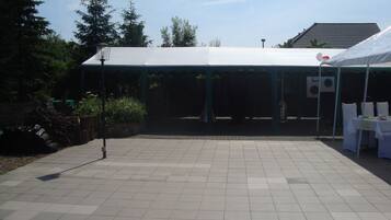 A covered outdoor area with a tiled floor, a white tent, and a building in the background.