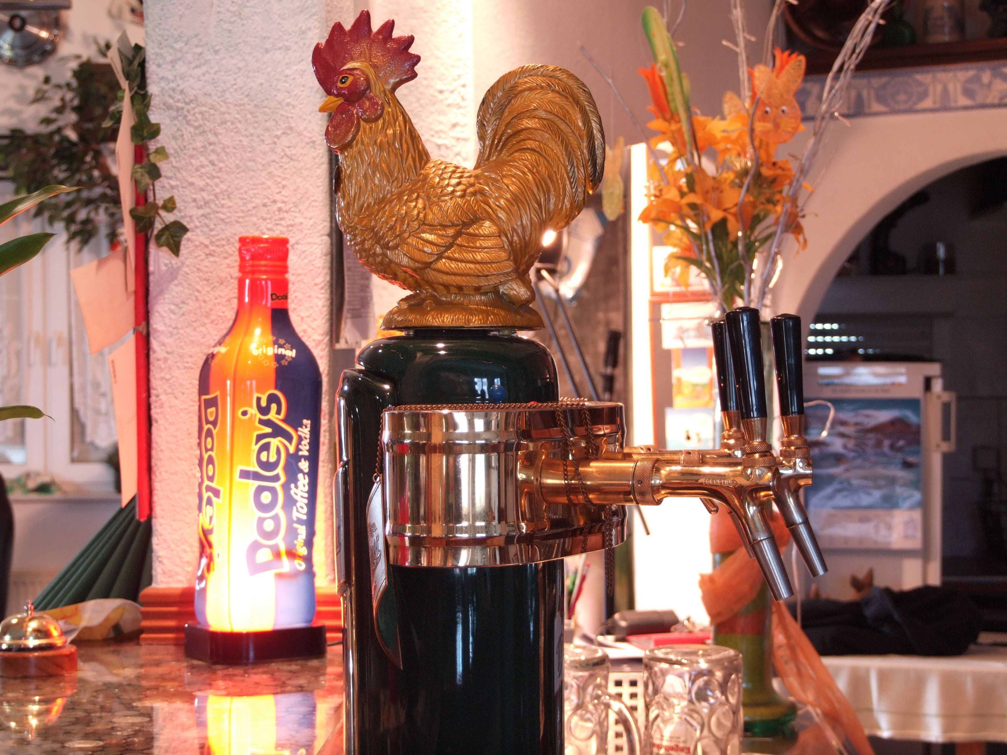 Un coin bar agrémenté d’un robinet décoratif en forme de coq, d’une bouteille de Dooley’s et d’un vase rempli de fleurs.