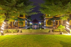 Un hotel bien iluminado con un patio central, rodeado de exuberante vegetación y un quiosco tradicional.