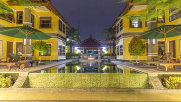 A courtyard with a pool, benches, and umbrellas, surrounded by yellow buildings with a central gazebo.