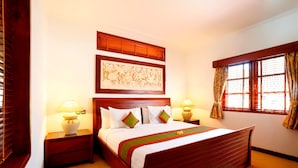 A neatly arranged bedroom with a wooden bed, two bedside tables with lamps, a large framed artwork above the bed, and a window with curtains. - Apel Villa Sanur (Denpasar)