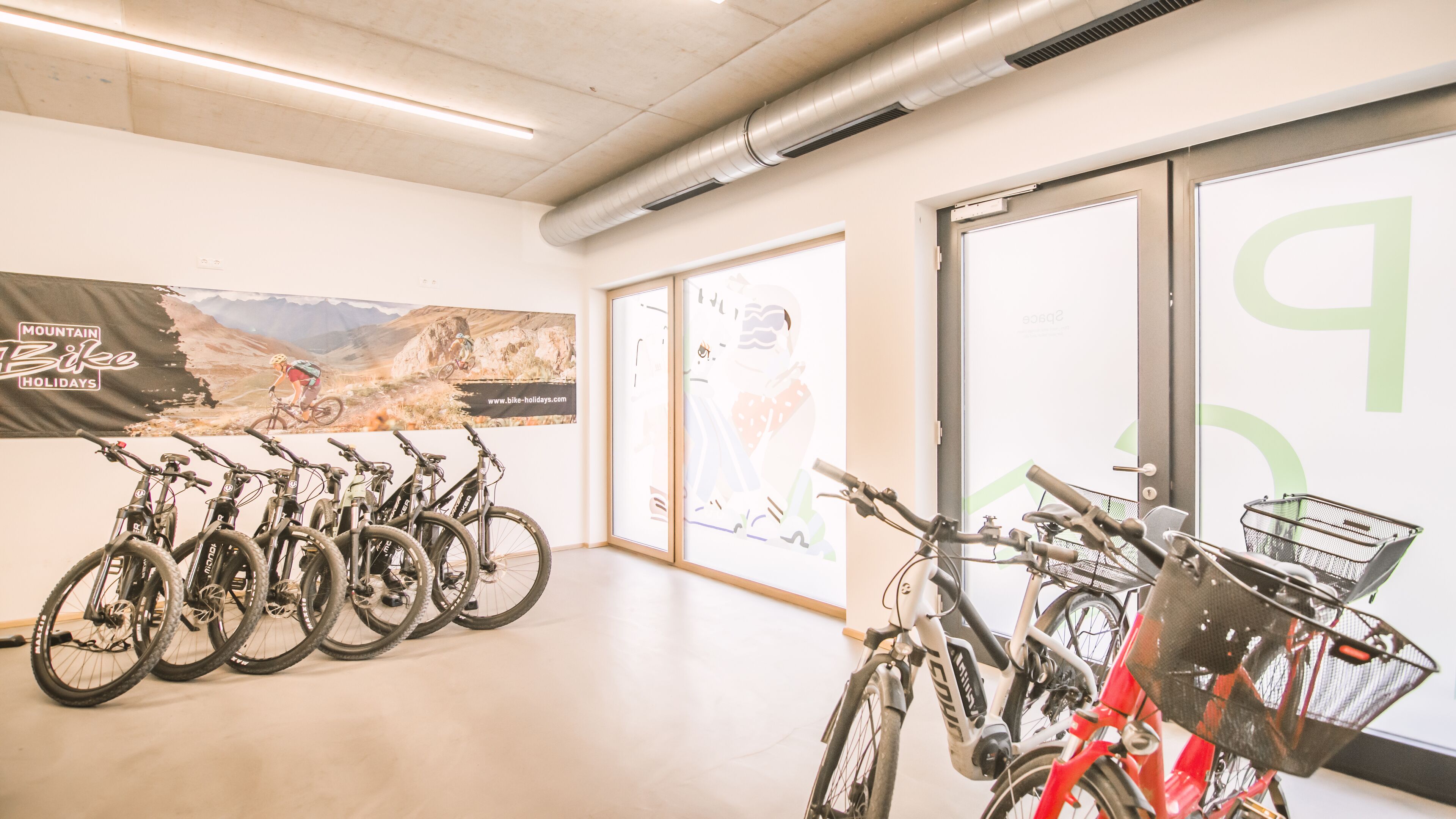 A bike rental station with several bicycles and a poster advertising mountain bike holidays.