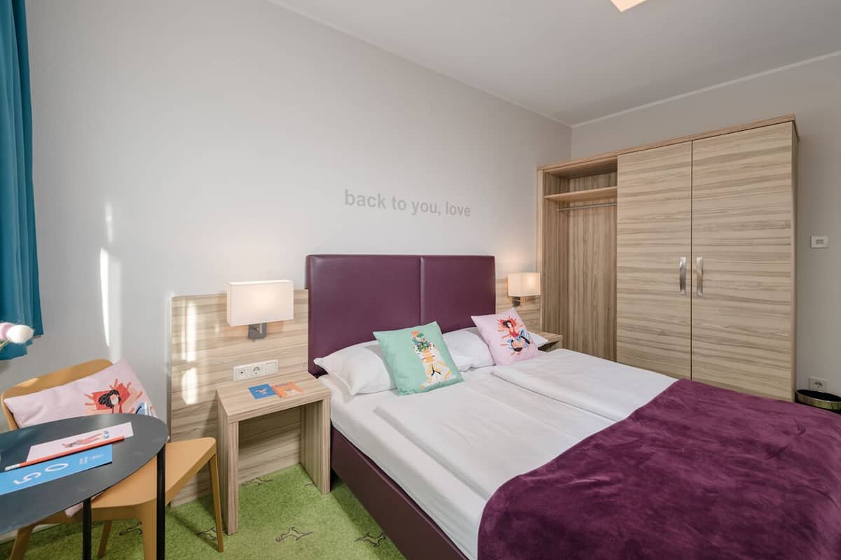 Habitación de hotel con cama, escritorio, silla, armario y una pared con un mensaje.