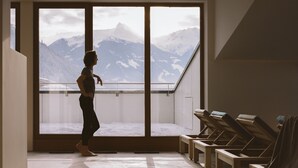 A room with a large window overlooking a snowy mountain landscape. There are wooden lounge chairs along the window.