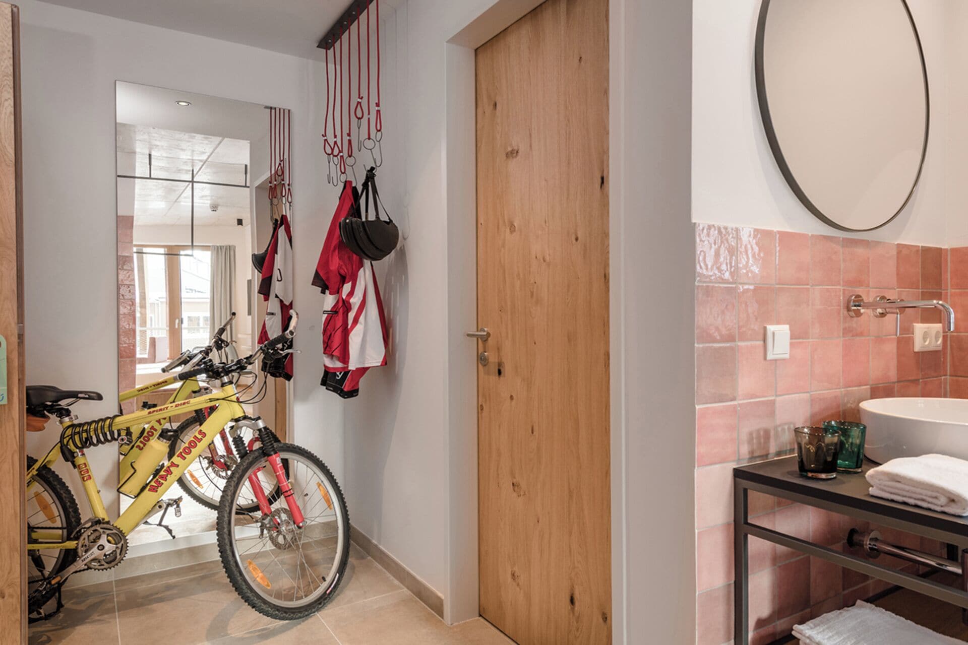 Ein Flur mit einem gelben Fahrrad, einer Holztür und einem Badezimmer mit Waschbecken und Spiegel.