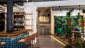 Zona de bar con estantes llenos de botellas, un letrero de neón y una silla verde.