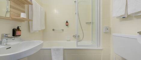 Un baño con lavamanos, inodoro y ducha. Hay toallas y un dispensador de jabón en la pared.