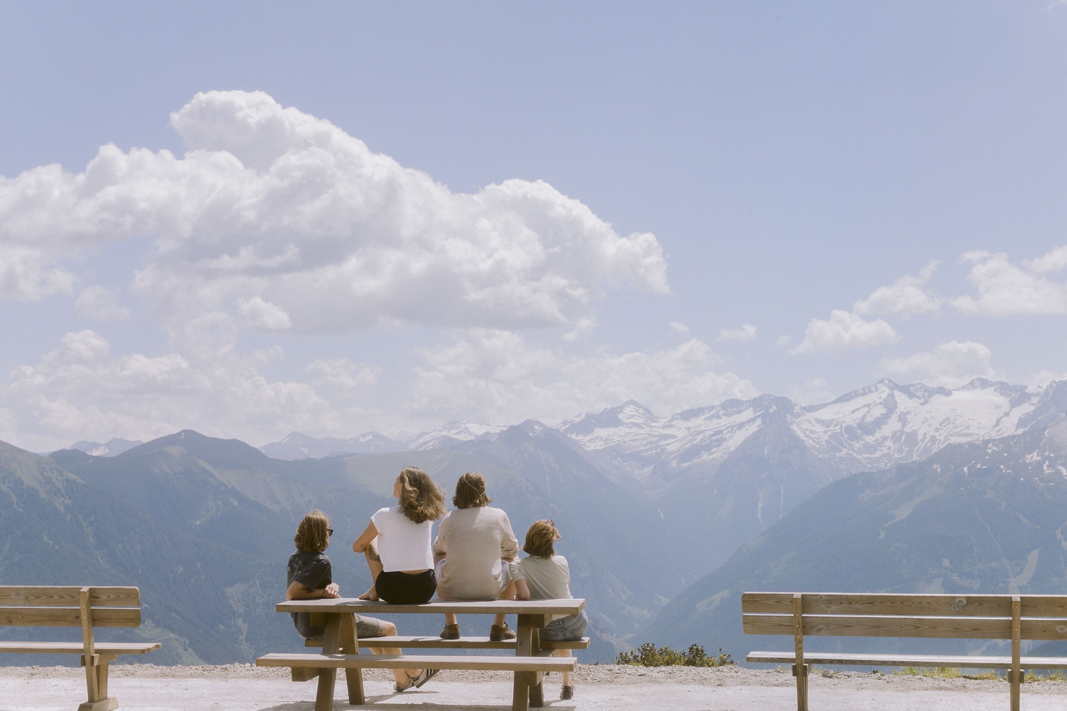 A group of people sitting on wooden benches facing a mountainous landscape.