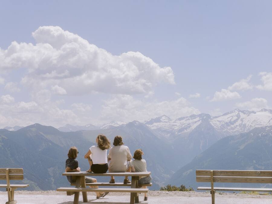 Un grupo de personas sentadas en bancos de madera mirando un paisaje montañoso.