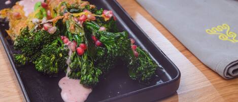 A black tray with food, including broccoli and pomegranate seeds, on a wooden table.
