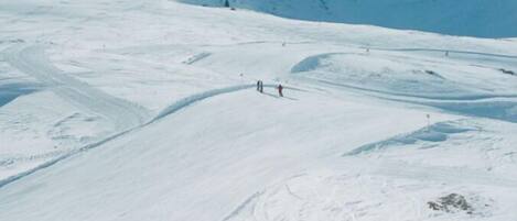 Une pente de montagne enneigée, avec des skieurs et un ciel dégagé.