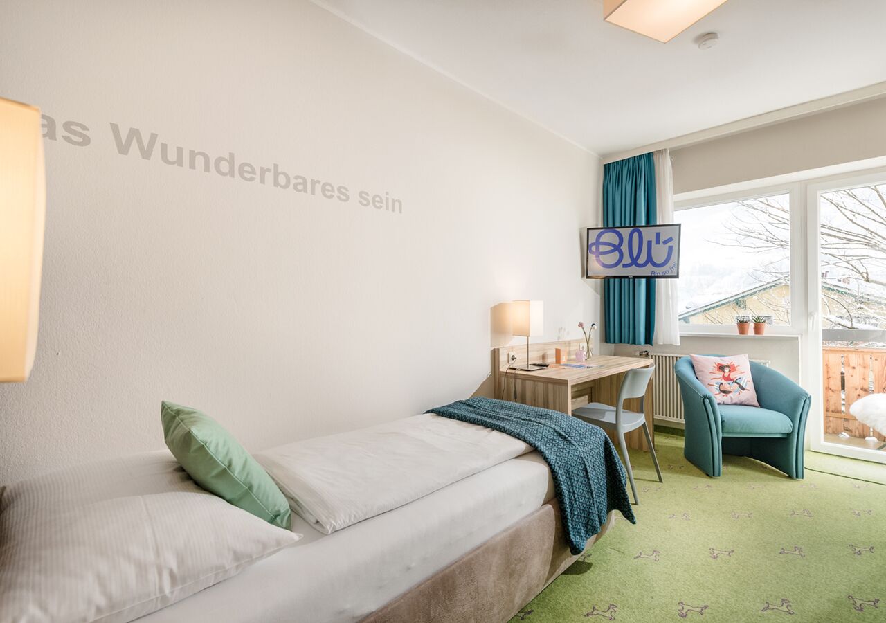 Une chambre d’hôtel avec un lit, un bureau, une chaise et une fenêtre avec des rideaux.